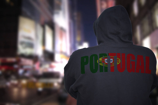 perigoso homem de pé em uma rua da cidade à noite com capuz preto com texto portugal em suas costas
 - Foto, Imagem