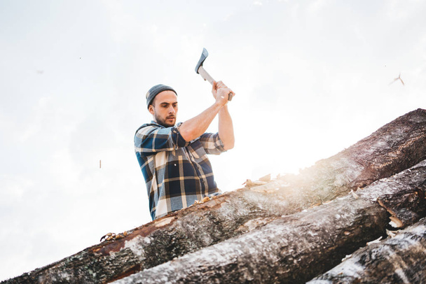 Strong lumberjack holds ax with both hands and cuts large tree, chips fly away - Valokuva, kuva