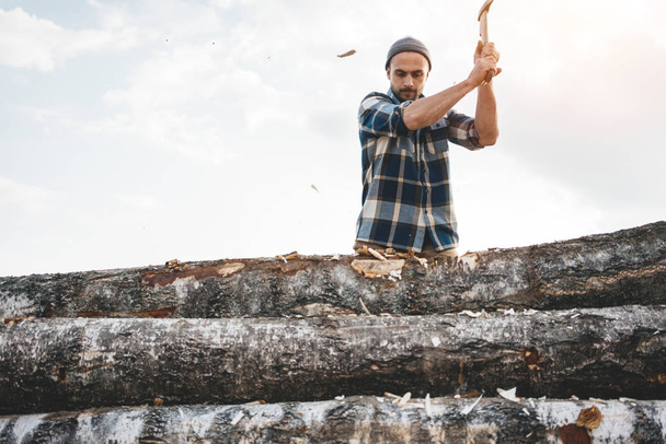 Professional strong lumberjack work on sawmill and sawing big tree with ax. Wooden chips fly apart - Photo, image