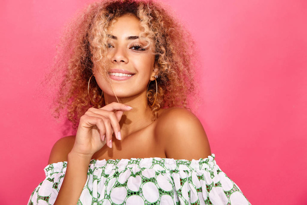 Portrait of blissful lovable woman with blond african hairstyle smiling and looking on camera. Girl in trendy summer clothes posing on pink background - Fotografie, Obrázek