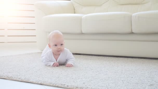 Bebé feliz acostado en el fondo de la alfombra, niña sonriente con ropa blanca
 - Imágenes, Vídeo