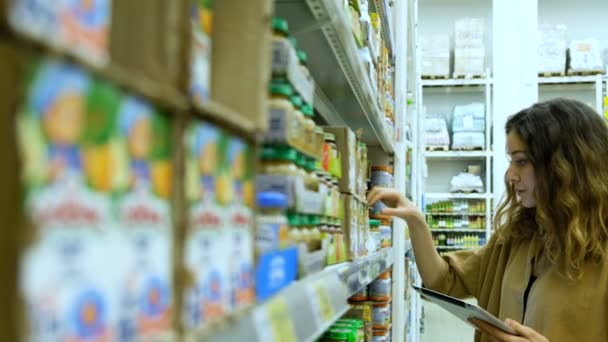 Nuori nainen, jolla on tabletti, ostaa vauvanruokaa supermarketissa, tyttö tutkii huolellisesti tuotteen koostumusta.
 - Materiaali, video