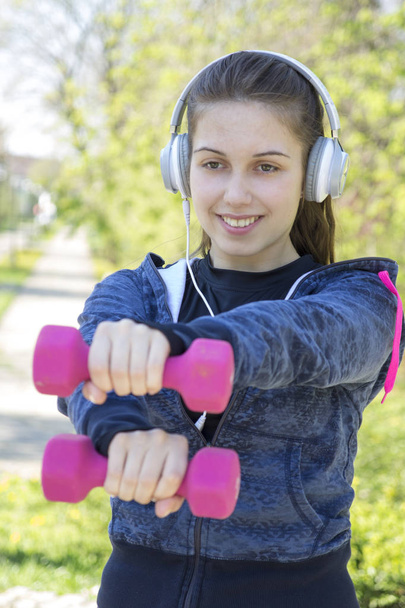 Beautiful young woman doing exercise with weights in the park. Selective focus and small depth of field. - Fotoğraf, Görsel