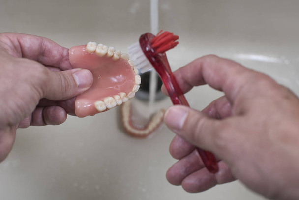 denture cleaning with brush in the sink with running water - Photo, Image