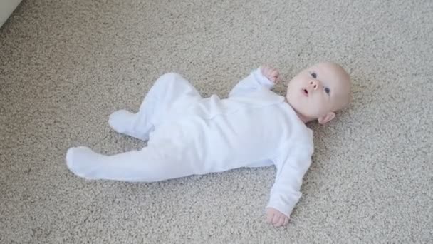 Happy Baby leží na koberci pozadí, usmívající se dítě dítě dívka v bílém oděvu uvnitř - Záběry, video