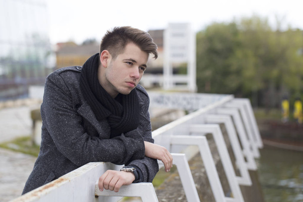 Hezký a atraktivní mladý muž opřený o kovový plot a čekání - Fotografie, Obrázek
