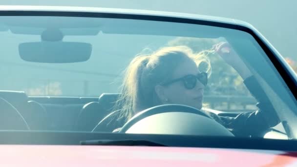 Portret: mooie meisje in zwarte bril en lederen jas in een rode cabriolet tegen de achtergrond van de hoge bergen. - Video