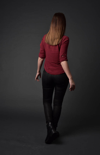 retrato de longitud completa de chica morena con camisa roja y pantalones de cuero. pose de pie, sobre fondo gris estudio
. - Foto, Imagen
