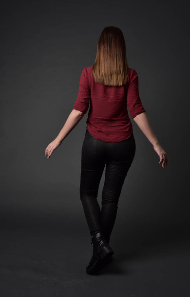 Pełna długość Portret brunetka dziewczyna ubrana w czerwoną koszulę i Spodnie skórzane. pozie stojącej, na studio szary tło. - Zdjęcie, obraz