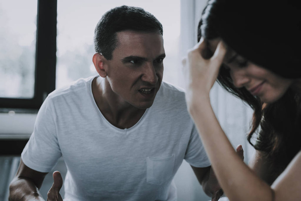 Angry Husband Screams at Wife During Quarrel. Woman Holds Head with Hand Has Conflict with Man at Home. Married Couple Sitting on Bed and Arguing. Family Relationship Problems and Misunderstanding - Zdjęcie, obraz