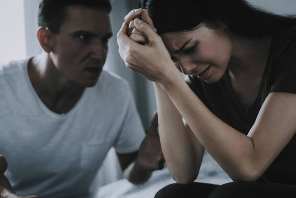 Angry Husband Yells at Wife During Quarrel. Crying Woman Holds Head with Hands Has Conflict with Man at Home. Couple Sitting on Bed and Arguing. Family Relationship Problems and Misunderstanding - Φωτογραφία, εικόνα