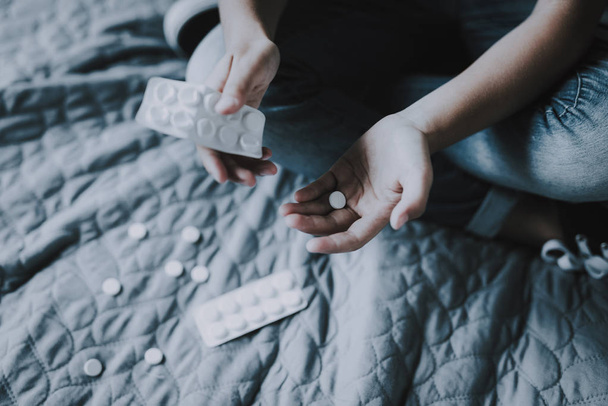 Closeup of Child Hands Holds Pills Sits on Bed with Crossed Legs. Closeup of Little Girl with Tablets Scattered around Sitting on Gray Badcover Near Opened Packing of Medicines - Φωτογραφία, εικόνα