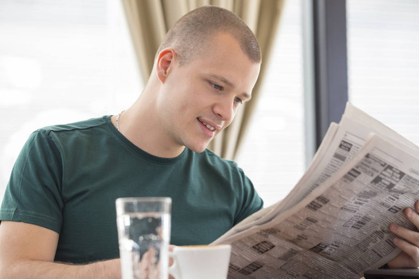 Νεαρός άνδρας κάθεται σε ένα τραπέζι και να διαβάσετε εφημερίδες και δουλειά αναζήτησης - Φωτογραφία, εικόνα