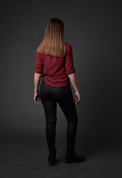 Portret van de volledige lengte van brunette meisje rood shirt en lederen broek dragen. staande pose, op grijs studio achtergrond. - Foto, afbeelding