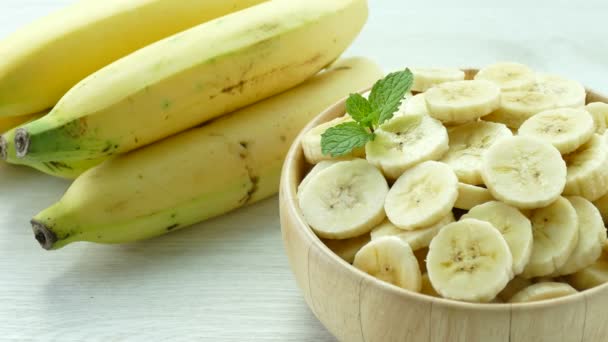 sliced bananas in wooden bowl and whole bananas on table  - Footage, Video