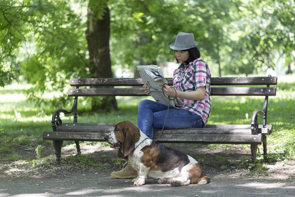 Ella ama a su perro. Una mujer se sienta en un banco en el parque con su hermoso perro y leyendo el periódico y relajarse
. - Foto, Imagen