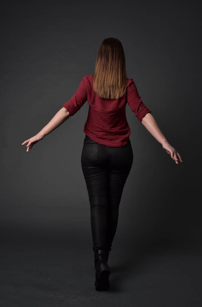 Ganzkörperporträt eines brünetten Mädchens in rotem Hemd und Lederhose. Stehende Pose, auf grauem Studiohintergrund. - Foto, Bild