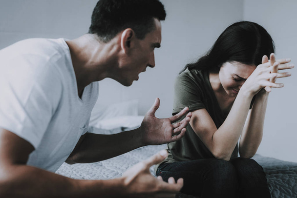 Angry Husband Yells at Crying Wife During Quarrel. Woman Holds Head with Hands Has Conflict with Man at Home. Couple Sitting on Bed and Arguing. Family Relationship Problems - Фото, зображення