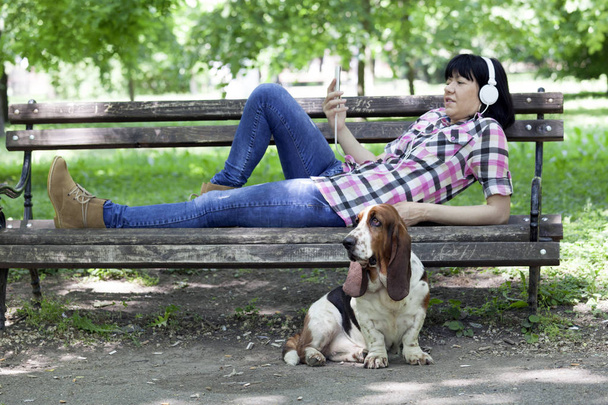 Woman with her dog resting on a bench and listen to music. Selective focus and smal depth of field - Фото, изображение