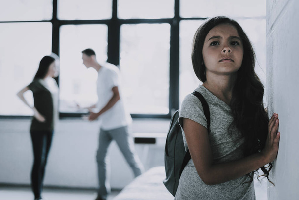 Sad Girl Listens How Parents Arguing at Home. Portrait of Child Looks Gloomy Leaning Against Wall While Mother and Father Scolding in Living Room on Backround. Family Relationship Problems Concept - 写真・画像