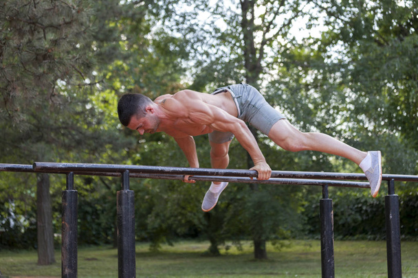 Young muscular young man doing exercises on the parallel bars in the park - Photo, Image