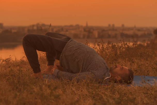 Людина робить йоги на захід сонця з видом на місто, Setu Bandha Sarvangasana/підтримувані міст Posetoned зображення. - Фото, зображення