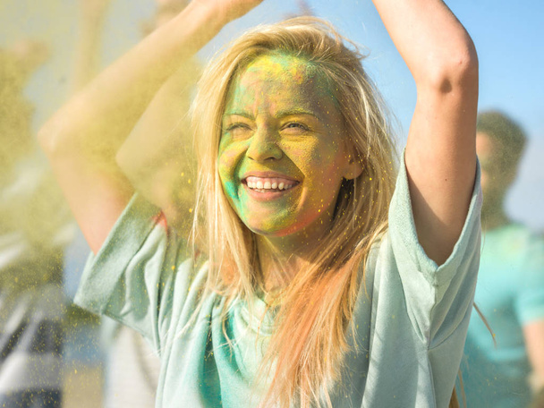 Portrait of a Beautiful Blonde Girl Dances in Celebration of Holi Festival With Her Friends. Her Face and Clothes are Covered with Colorful Powder. - Fotografie, Obrázek