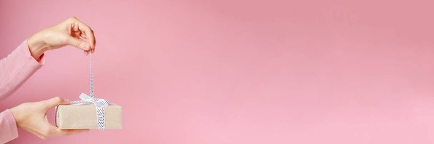 donna mani slegare fiocco su scatola regalo su sfondo rosa, lungo banner con spazio copia
 - Foto, immagini