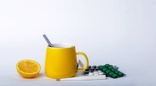 Una taza amarilla de té con limón, un termómetro y pastillas para el tratamiento del resfriado y la gripe. Prevención de resfriados y gripe sobre fondo gris
 - Foto, Imagen