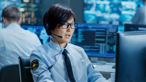 In the Security Command Center Officer at His Workstation Monitors Screens and Communicates with Patrols through Headset. He is Part of the Surveillance Team. - Photo, Image