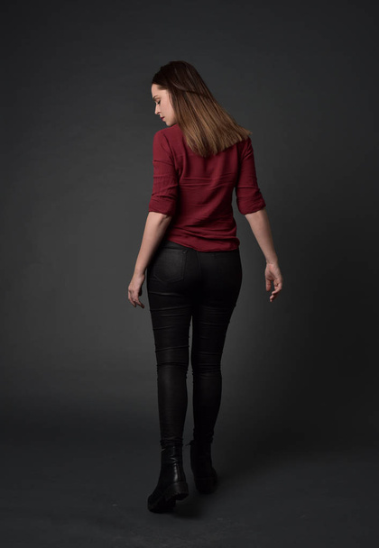 Ολόσωμο πορτρέτο μελαχρινή κοπέλα φορώντας κόκκινο πουκάμισο και δερμάτινο παντελόνι. όρθια στάση, σε φόντο γκρι στούντιο. - Φωτογραφία, εικόνα