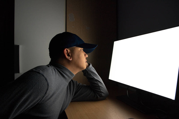 Widok z boku człowieka Hacker siedzieć przy monitorze komputera. w ciemnym pokoju. - Zdjęcie, obraz