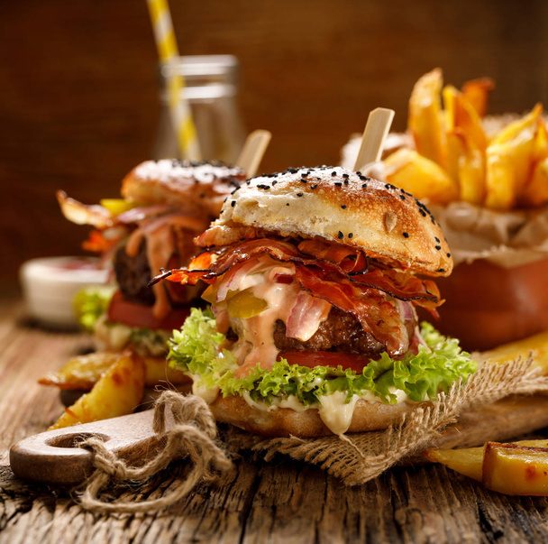 Čerstvé burger s grilovanou slaninou, červenou cibulkou, čerstvý hlávkový salát, naloženými okurkami, rajčaty a aromatického sýra na dřevěném prkénku.  - Fotografie, Obrázek
