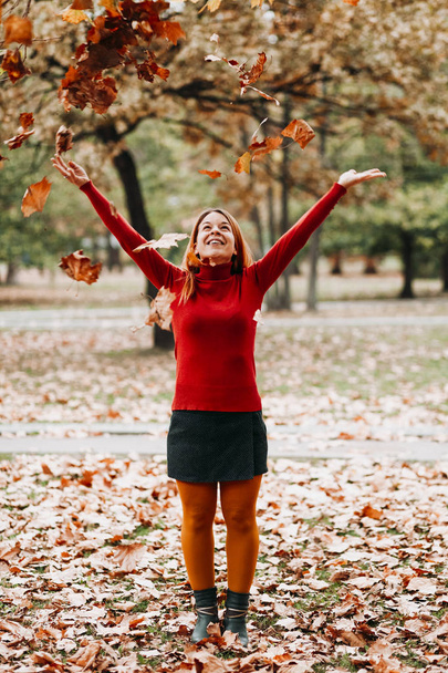 Jonge vrouw gooien herfst bladeren in de lucht in het park - Foto, afbeelding