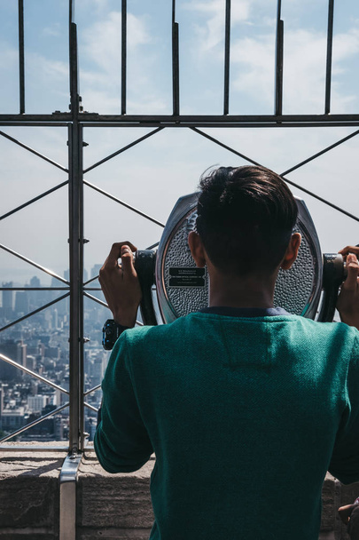 New York, USA - May 29, 2018: Young man looking using binoculars on the observation platform at Empire State Building, New York. New York is one of the most visited cities in the world. - Foto, imagen
