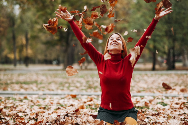 秋を投げる若い女性が公園で空気の葉します。 - 写真・画像