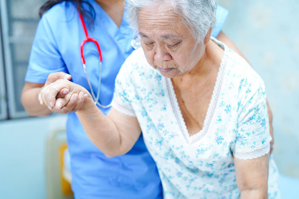 Ázsiai nővér gyógytornász orvos ellátás, a Súgó és támogatás a vezető vagy az idős hölgy nő beteg kap fel az ágyból a kórházi osztályon: egészséges, erős orvosi koncepció. - Fotó, kép