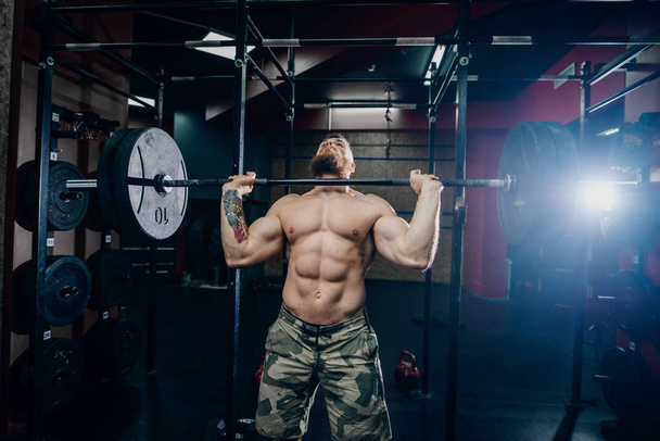 Bearded guy with six-pack lifting barbell in crossfit gym. Weight plates in background. - Photo, Image