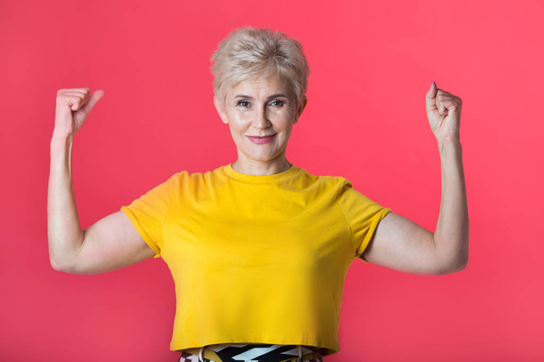 stylish woman at the age with a short haircut in a yellow T-shirt on a red background with a gesture of hands - Valokuva, kuva