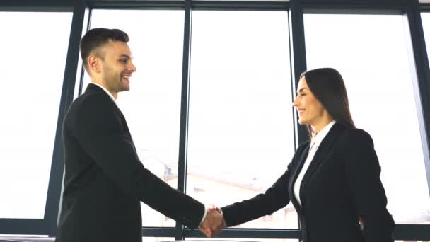 4К. Два бизнес-партнера, мужчина и женщина, с удовольствием пожимают друг другу руки при встрече в офисе
.  - Кадры, видео