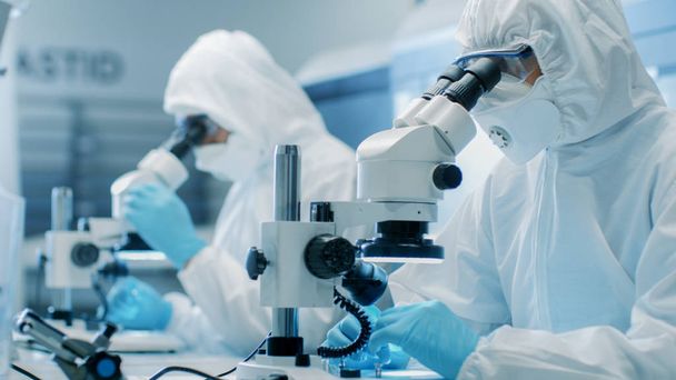 Two Engineers/ Scientists/ Technicians in Sterile Cleanroom Suits Use Microscopes for Component Adjustment and Research. They Work in an Electronic Components Manufacturing Factory. - Foto, Imagem