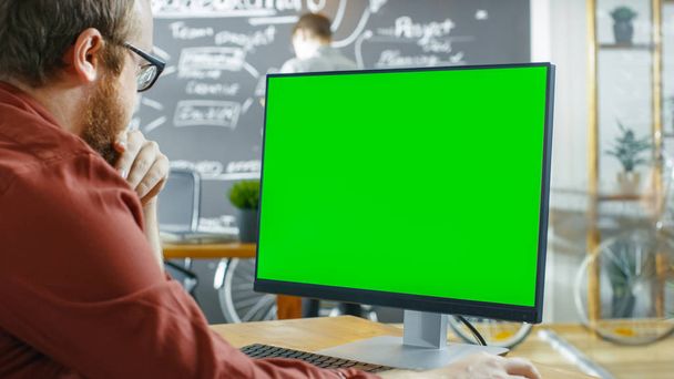 Man Works on the Personal Computer with Green Mock-up Screen. No fundo Escritório Criativo com Desenho de Homem na Parede Chalkboard
. - Foto, Imagem