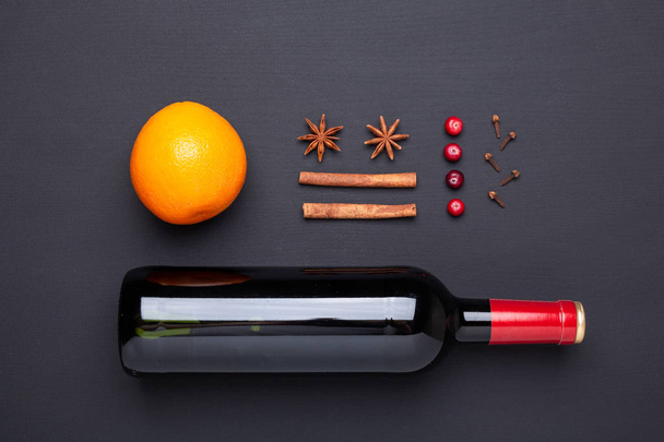 Bottle of red wine and spice for mulled wine on black background. Cinnamon, anise stars, orange, cranberries. Top view. - Foto, Imagem