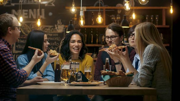 In the Bar/ Restaurant Group of Diverse Young People Eat Slices of Pizza Pie. They Talk, Tell Jokes and Have Fun in This Stylish Establishment. - Fotografie, Obrázek