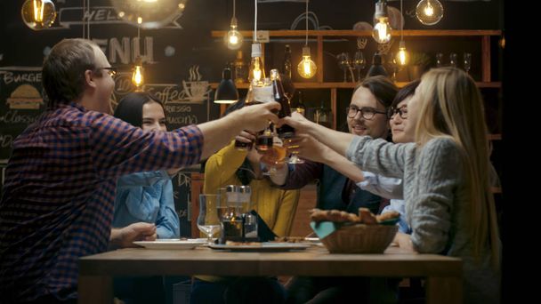 Diverse Group of Friends Celebrate with a Toast and Clink Raised Glasses with Various Drinks in Celebration. Beautiful Young People Have Fun in the Stylish Bar/ Restaurant. - Foto, Bild