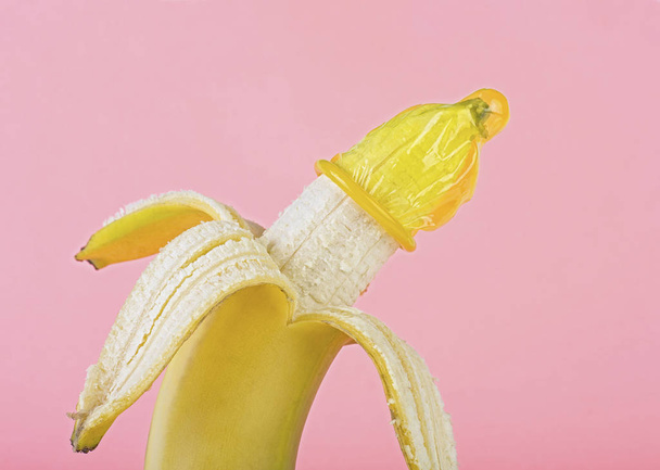 Safe sex concept - yellow condom on banana, pink background.  - Foto, Imagem