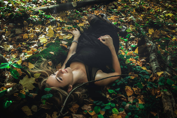 A young kind witch in a black dress with a black mask in a mystical forest in various poses. Art processing. - Fotografie, Obrázek