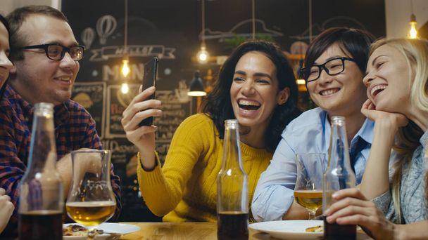 In the Bar/ Restaurant Hispanic Woman Makes Video Call with Her Friends. Group Beautiful Young People in Stylish Establishment. - Photo, image