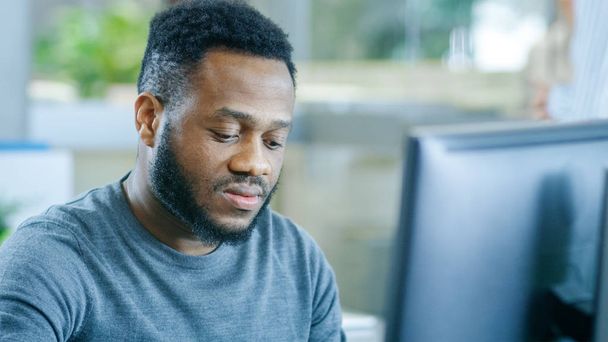 Young Black Man Diligently Works on a Personal Computer in the Corporate Office. Stylish Smart Man with a Trimmed Beard. - Fotoğraf, Görsel