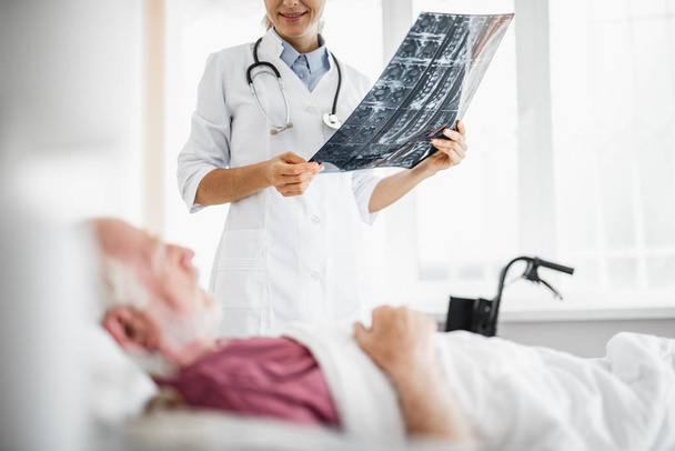 Doctor holding x-ray while looking at old man with smile - Foto, Bild
